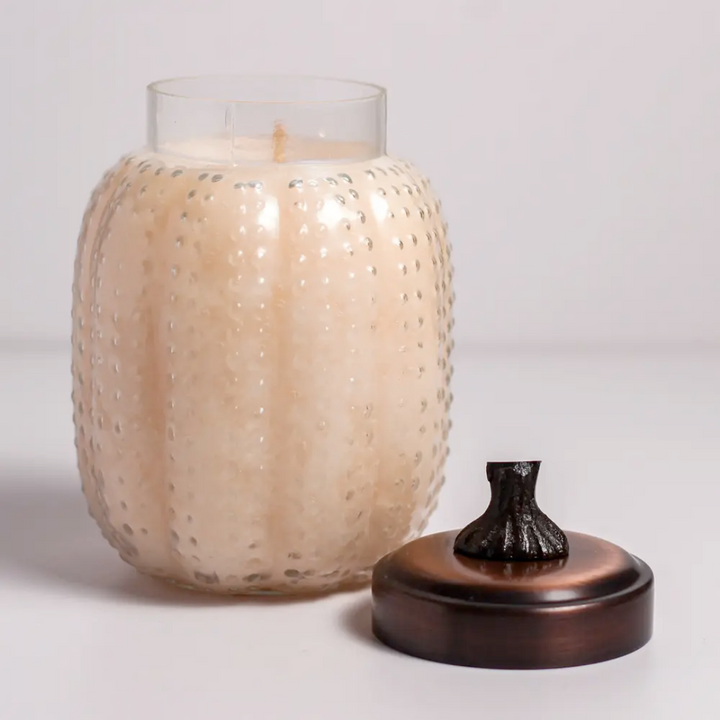 Candle in a textured glass holder with a bronze lid on a light gray background