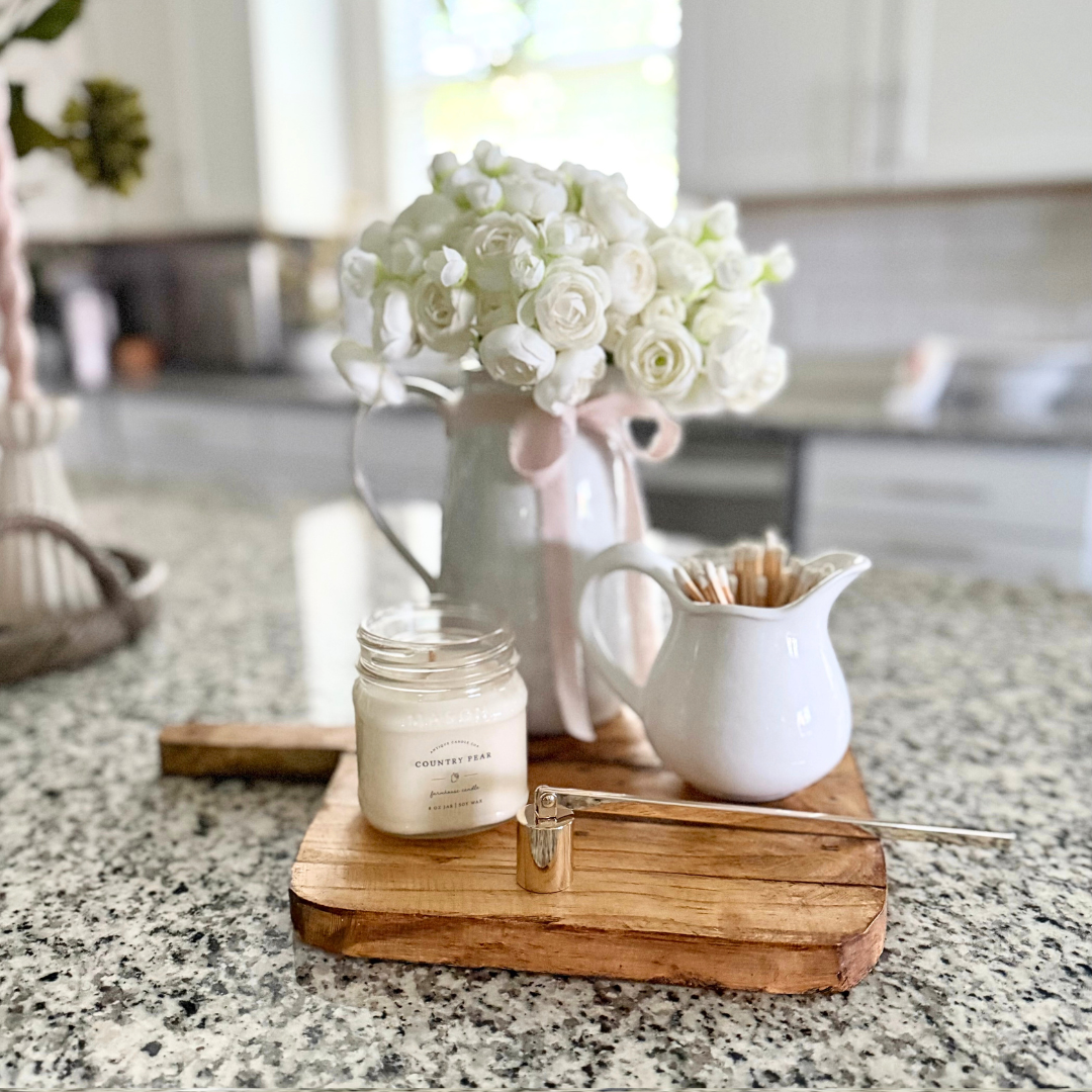 Candle, wooden decorative bread board, and white flowers on a kitchen counter
