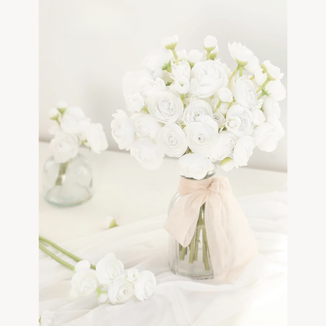 Bouquet of white ranunculus flowers in a glass vase with a pink ribbon on a light background