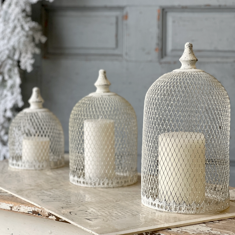 Decorative iron cloches with candles on a rustic wooden surface against a gray wall.