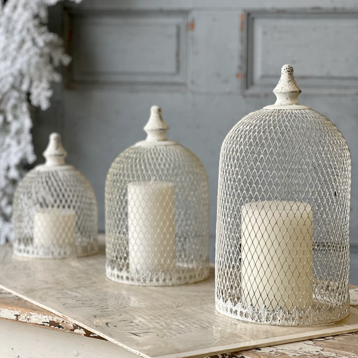 Decorative iron cloches with candles on a rustic wooden surface against a gray wall.