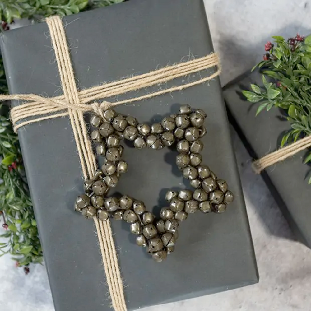 Gift wrapped in gray paper with a star-shaped jingle bell ornament and twine on a light background.