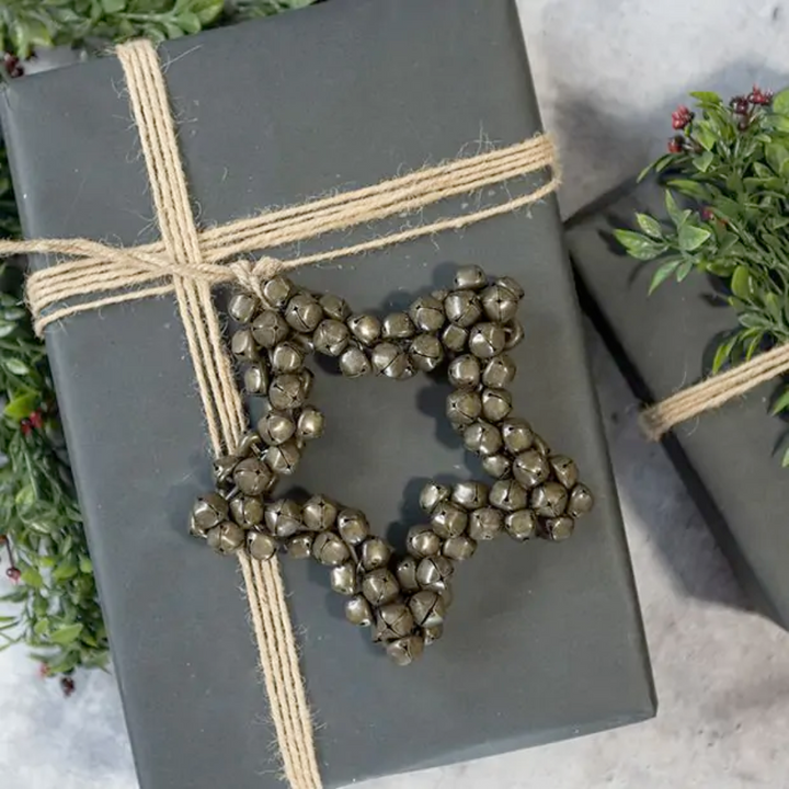 Gift wrapped in gray paper with a star-shaped jingle bell ornament and twine on a light background.