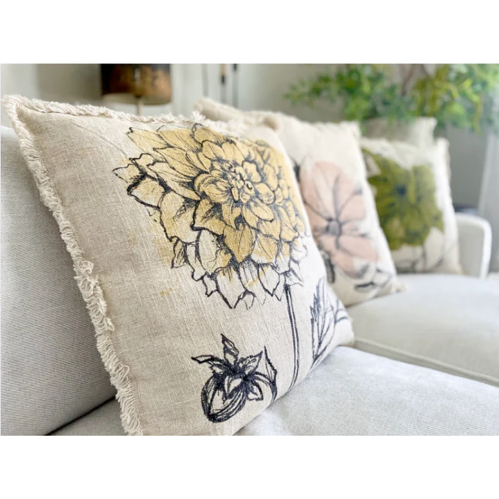 Linen pillow with yellow watercolor floral print design with a frayed trim edging, displayed on a bench.