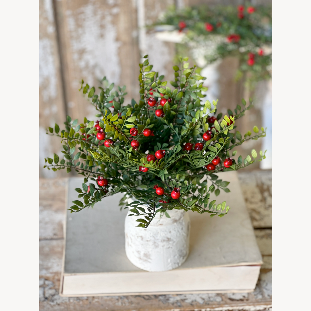 Artificial plant with red berries in a white pot on a wooden surface