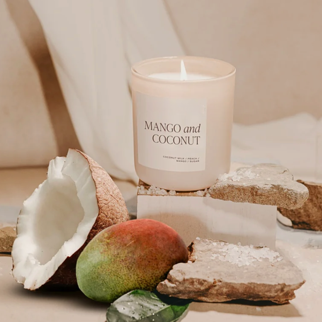 Candle labeled 'Mango and Coconut' with a mango and coconut shell on a neutral background