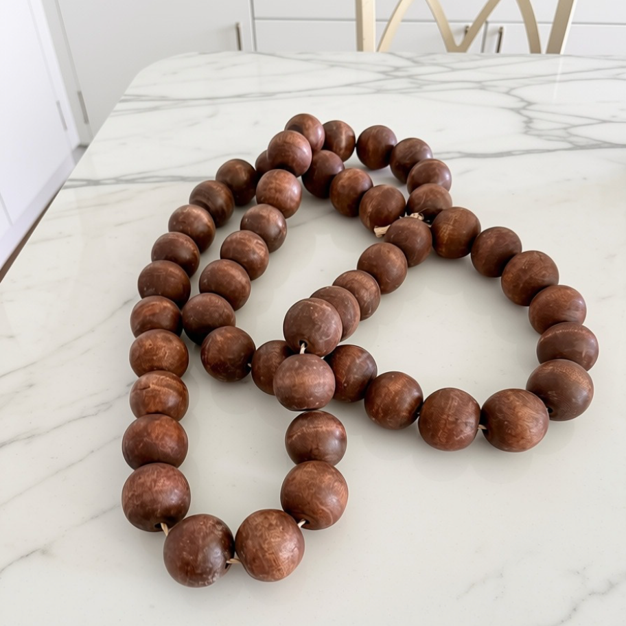 A long strand of large, round, medium-brown wooden beads arranged in loops on a white marble countertop.