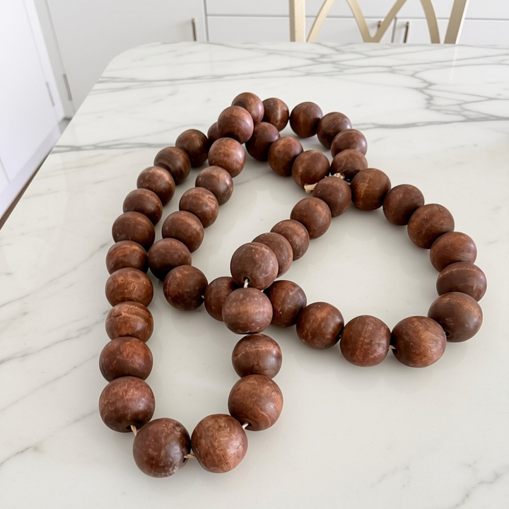 A long strand of large, round, medium-brown wooden beads arranged in loops on a white marble countertop.