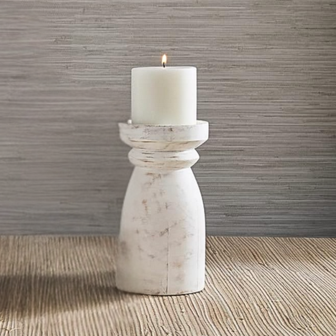White candle on a mango wood candle holder against a textured wall.