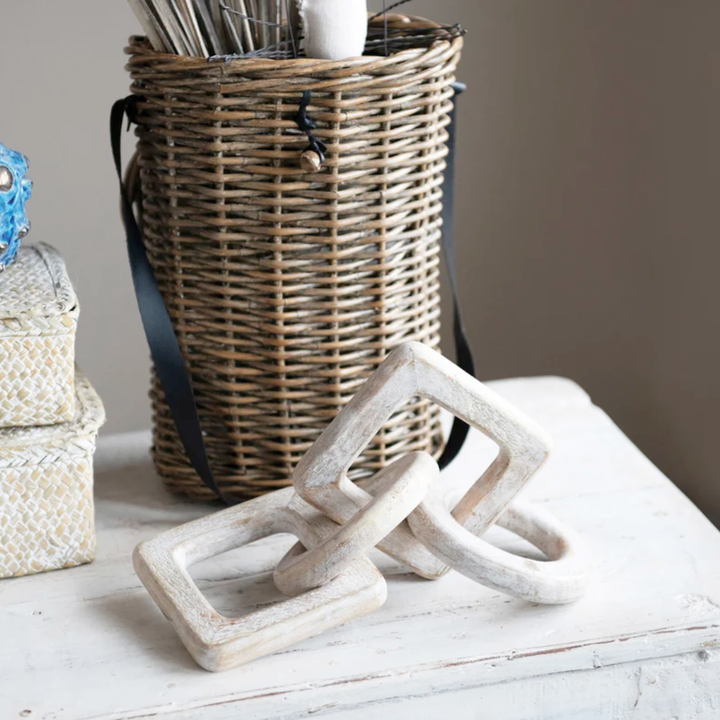 Decorative wooden chain link on a white surface with a wicker basket in the background.
