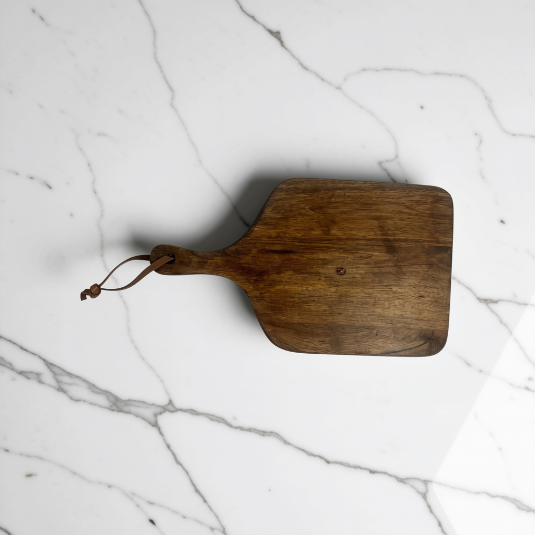 Set of two walnut brown wooden serving boards with leather handles resting on a white marble kitchen island.