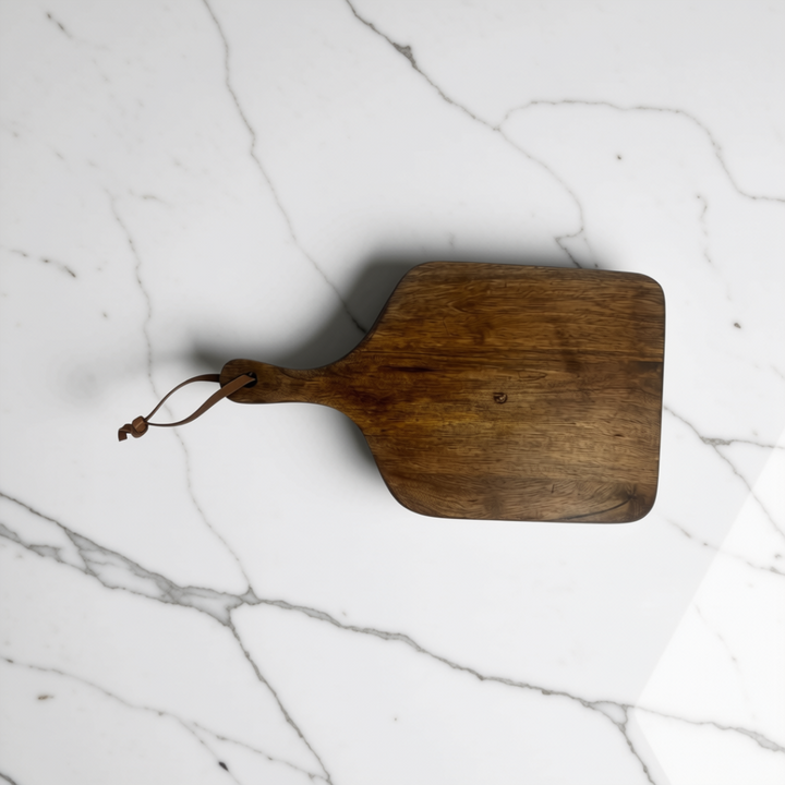 Set of two walnut brown wooden serving boards with leather handles resting on a white marble kitchen island.