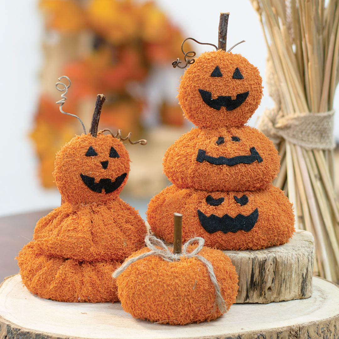 Stacked orange pumpkins with black faces on a wooden surface