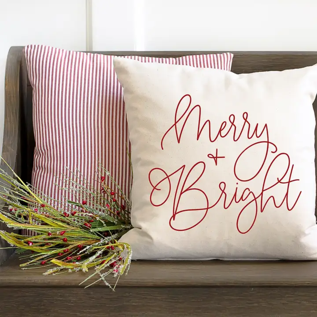 Decorative pillow with 'Merry & Bright' text on a wooden surface with a red and white striped pillow.