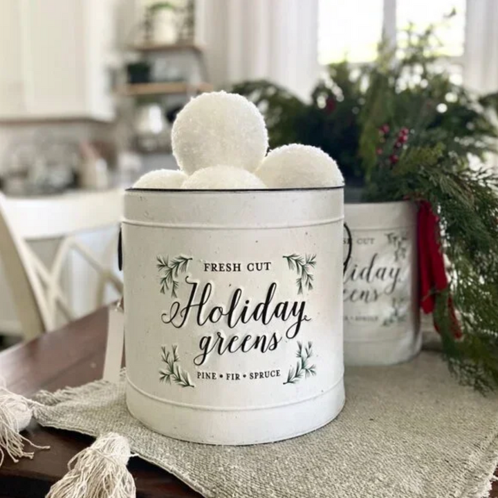 Decorative container labeled 'Fresh Cut Holiday Greens' with a blurred indoor background