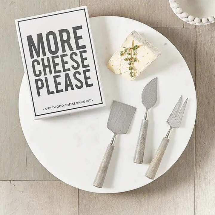 Driftwood cheese knife set with a block of cheese and a sign on a white plate.