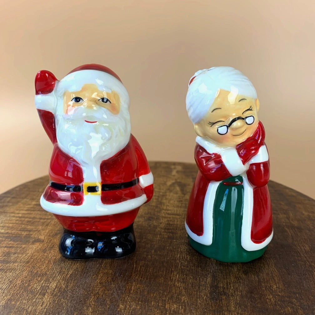 A ceramic salt and pepper set featuring hand-painted characters resembling Santa Claus and a Christmas-themed figure, primarily in red, white, green, and white colors.