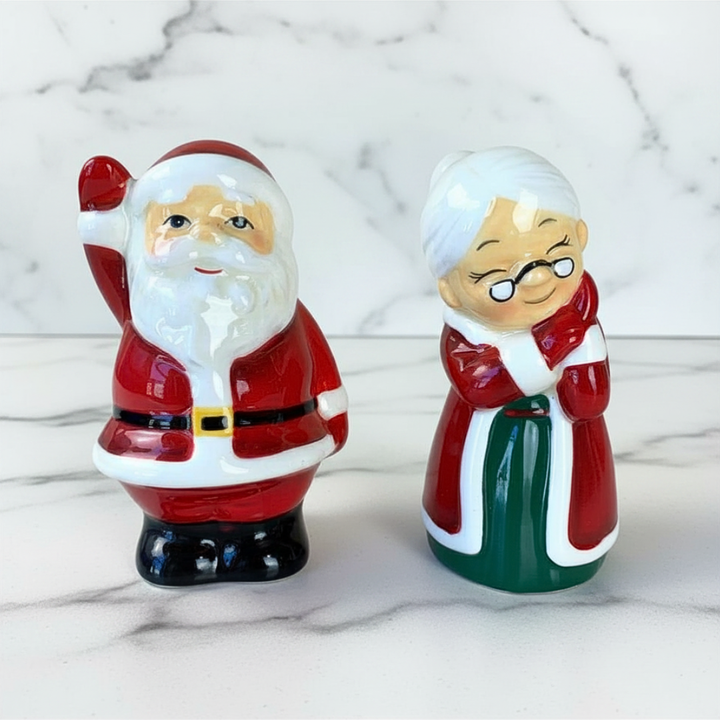 Two ceramic figures of Santa Claus and Mrs. Claus on a marble surface
