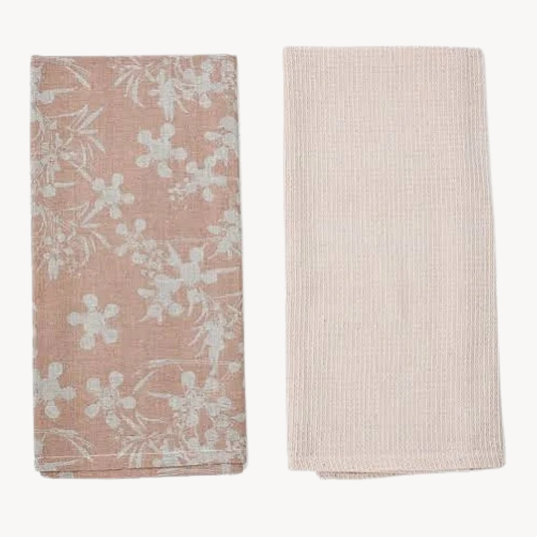 Two kitchen tea towels, one with a floral myrtle design and another in a solid honeycomb weave pattern, both in blush color.
