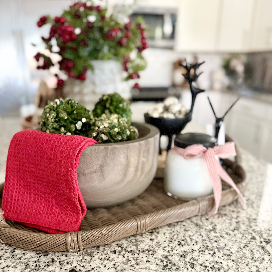Decorative tray with a wood bowl, red Christmas kitchen towel and candle on a countertop.
