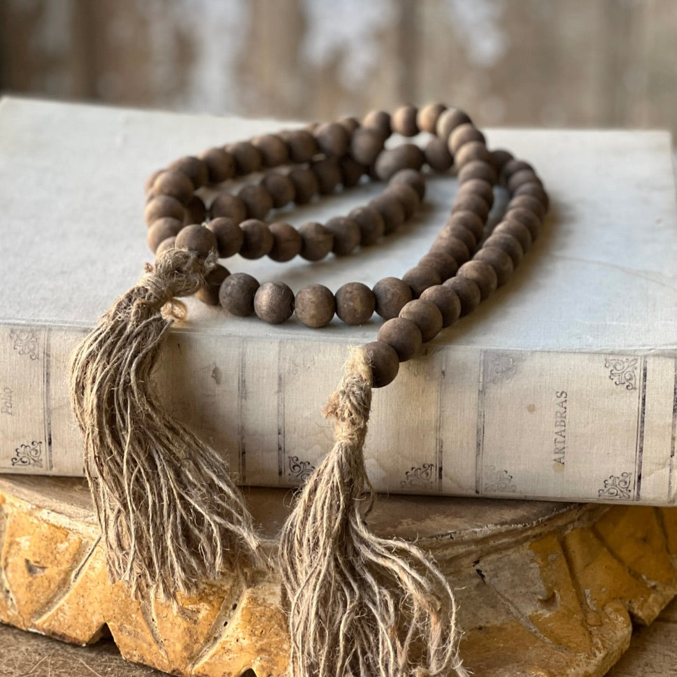 A brown wooden bead garland with tassels placed on a white surface.