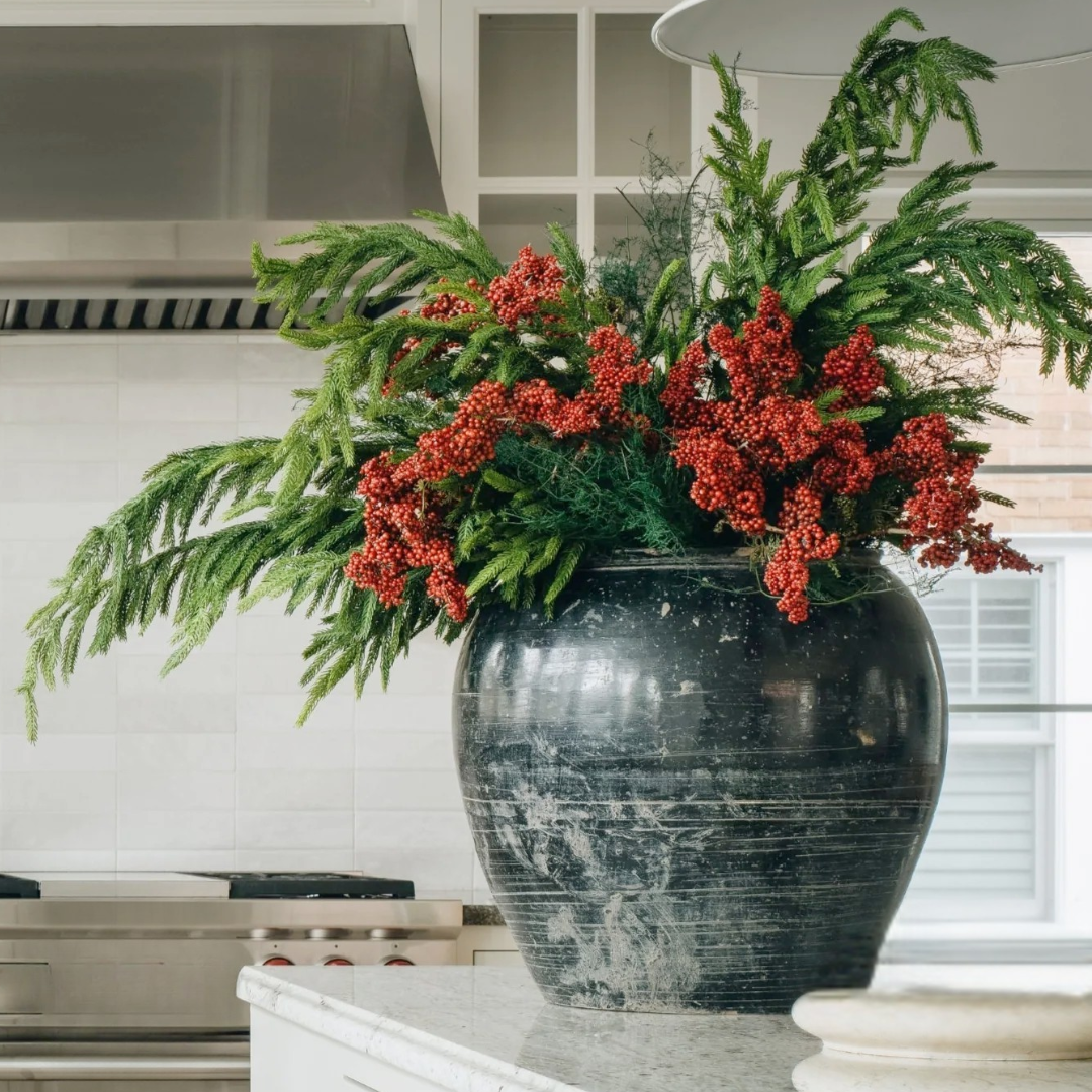 Decorative vase with green Norfolk Pine foliage and red berries on a kitchen counter