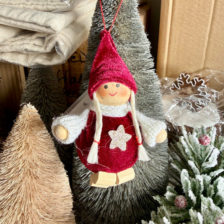 Decorative Christmas girl ornament with red hat and dress, surrounded by festive decorations.