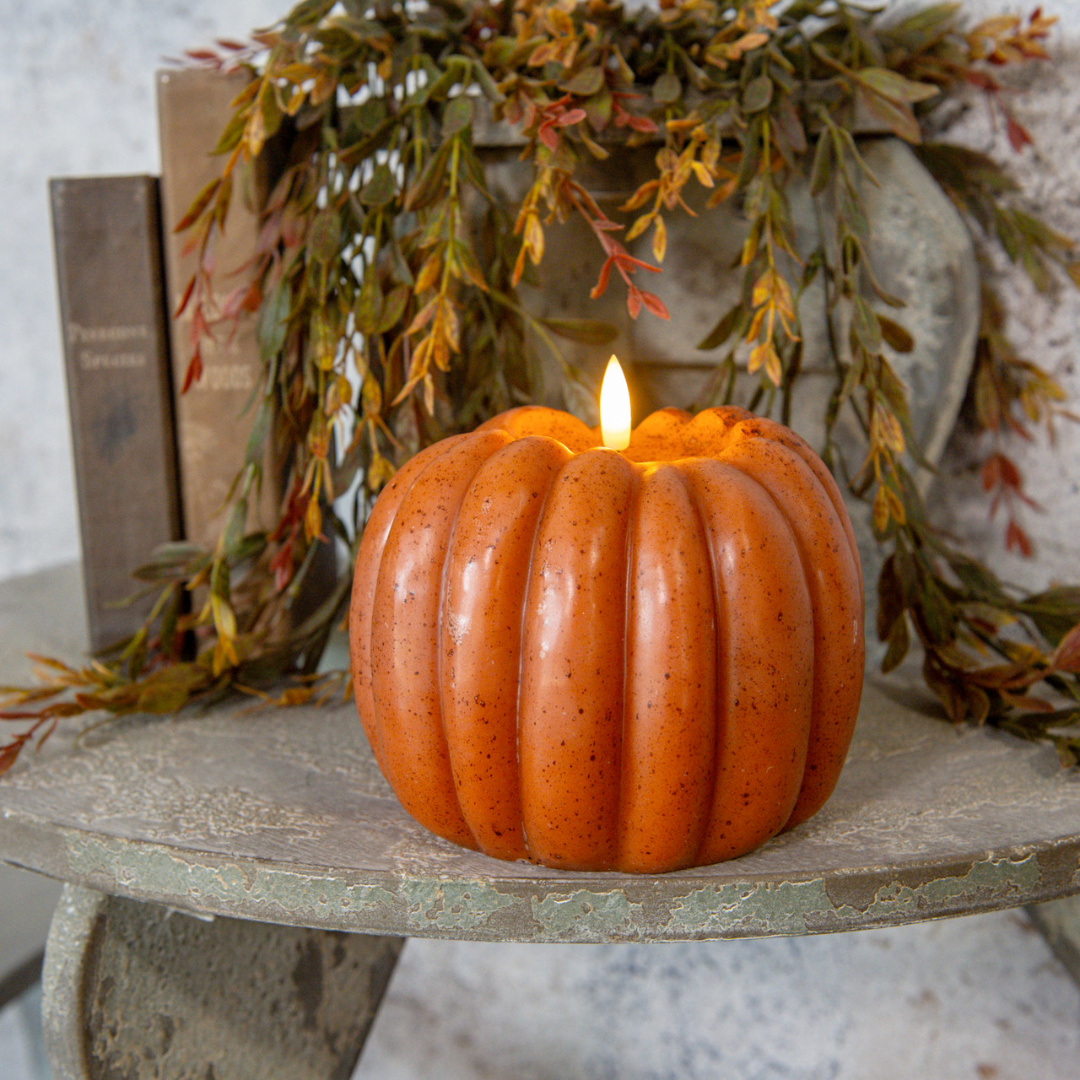 Decorative pumpkin candle on a rustic surface with greenery in the background