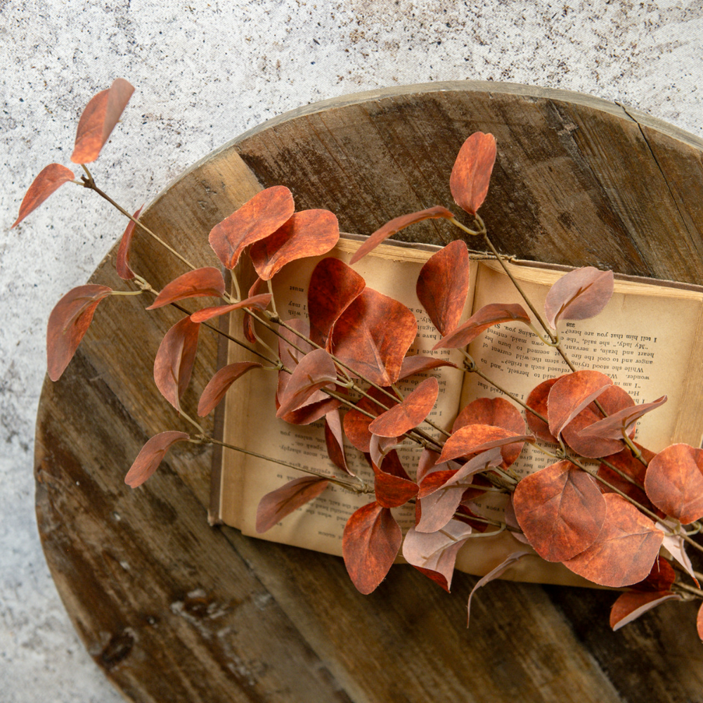Orange Faux Eucalyptus Leaf Sprays on an open book with a wooden surface underneath