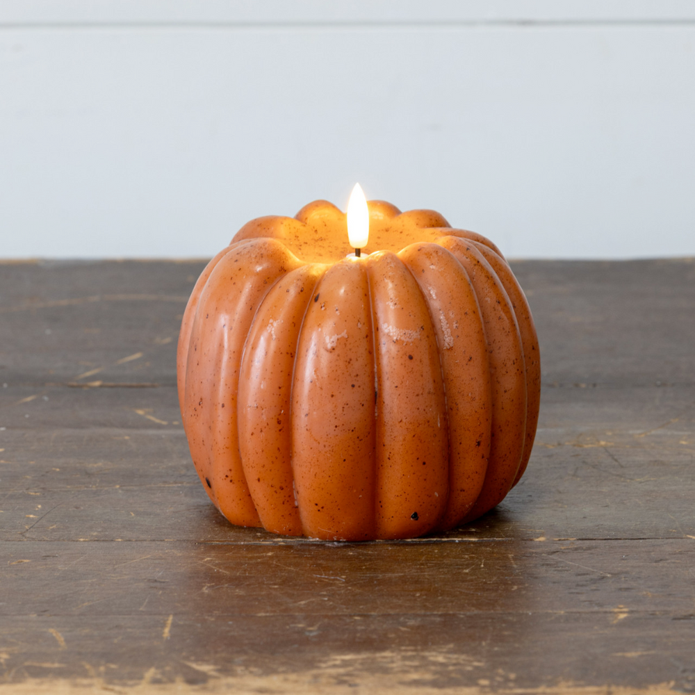 Pumpkin-shaped candle with a lit wick on a wooden surface