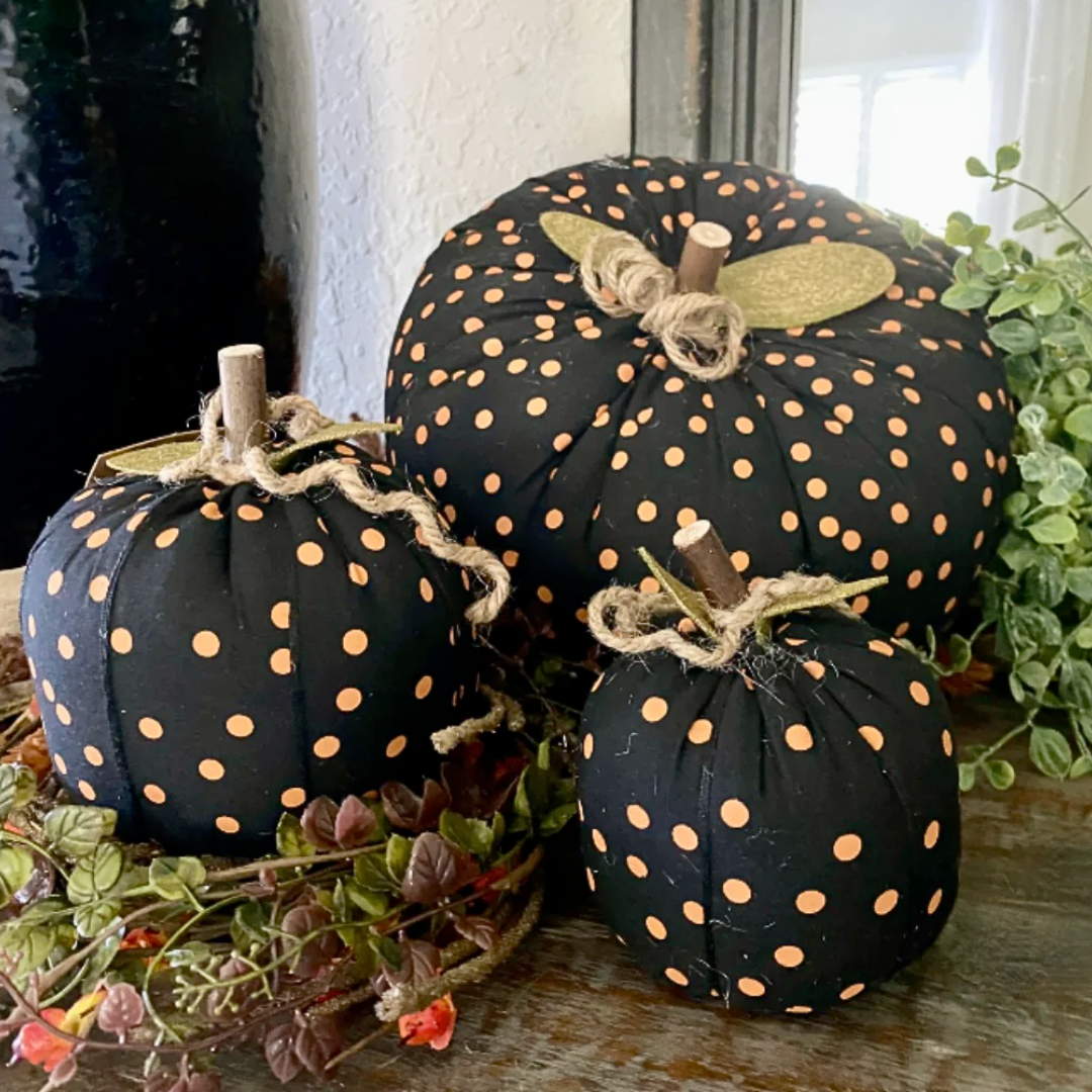 Black pumpkins with orange polka dots on a wooden surface with greenery.