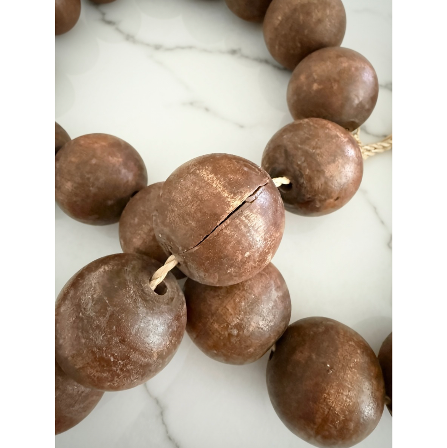 A close-up of dark brown wooden beads strung on a cord, with one bead showing a visible crack, set against a white marble background.