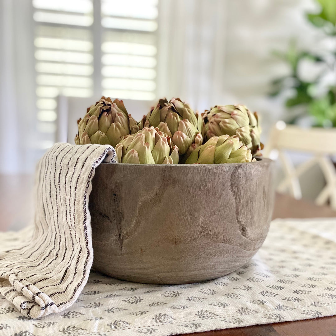 Paulownia wood dough bowl with faux artichokes and a farmhouse kitchen towel on a floral table runner