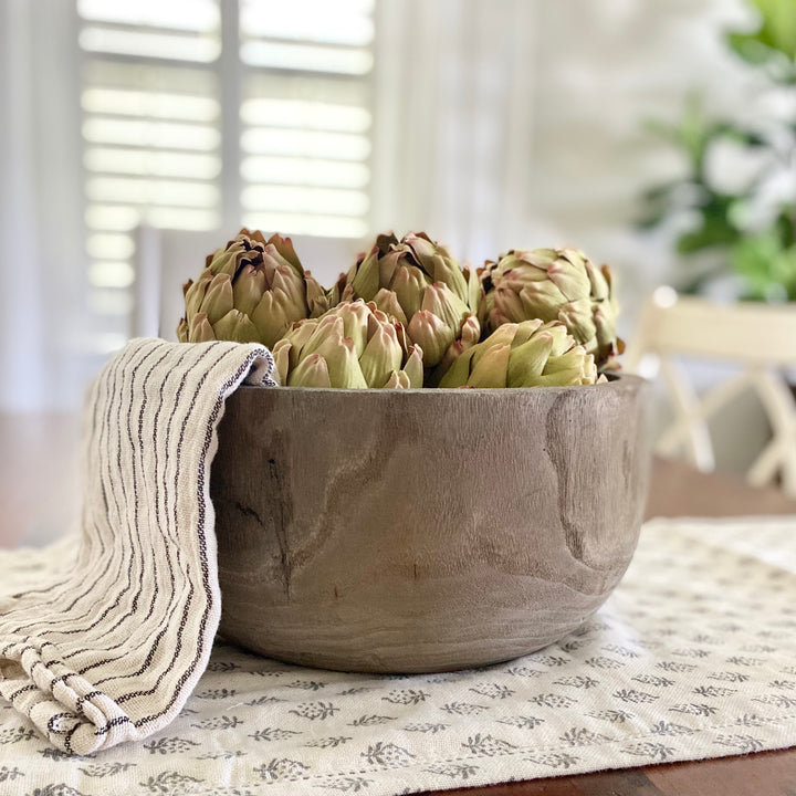 Paulownia wood dough bowl with faux artichokes and a farmhouse kitchen towel on a floral table runner