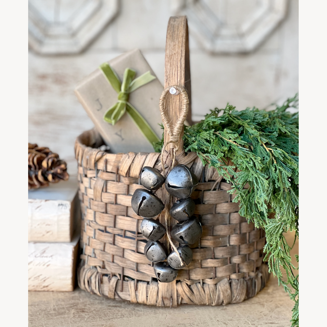 Woven basket with jingle bells and greenery on a wooden surface