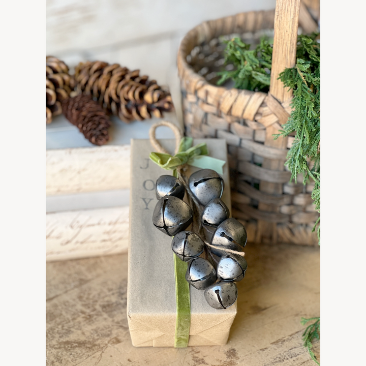Pewter metal jingle bells drop and green ribbon on a rustic background