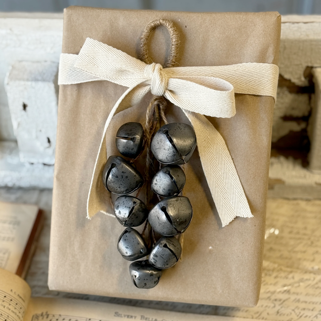 Gift wrapped in brown paper with a beige ribbon and metal pewter bells on a rustic background