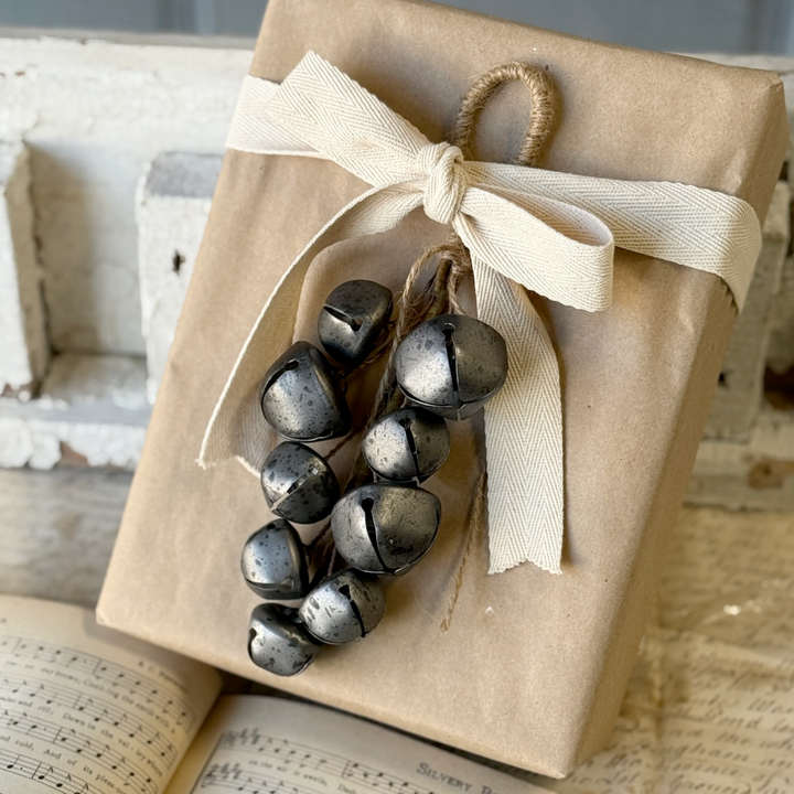 Gift wrapped in brown paper with a string of black jingle bells on an old book background