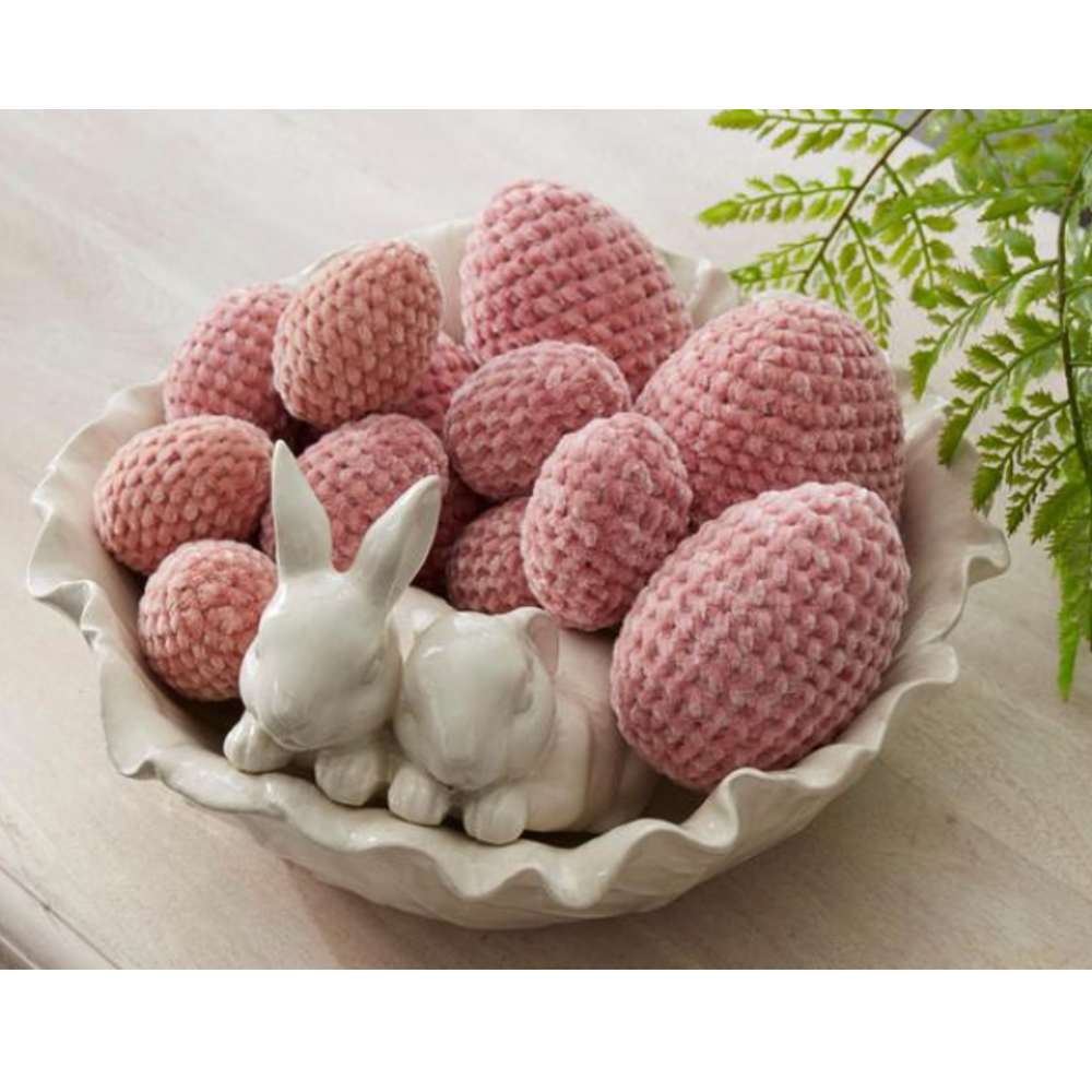 Pink crochet eggs in a decorative bowl with white rabbit figurines on a light background