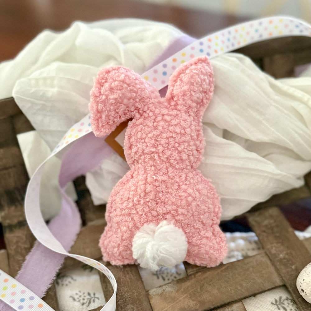 Pink textured Easter bunny with a white pom tail on a wooden surface