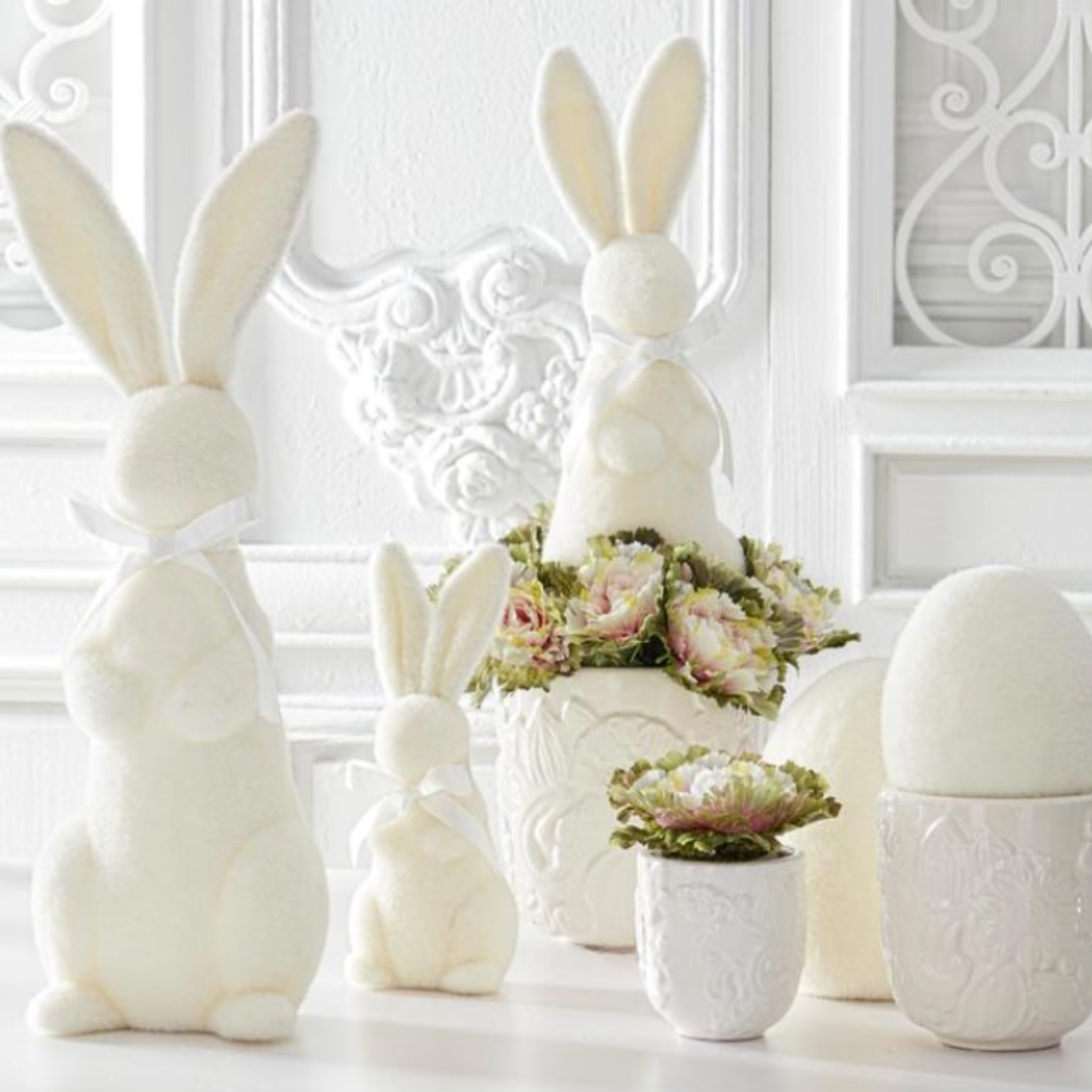 White ceramic bunny and egg decorations with floral arrangements on a white surface.