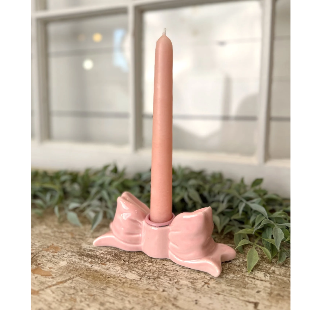 Pink candle holder with a pink candle on a wooden surface with greenery in the background