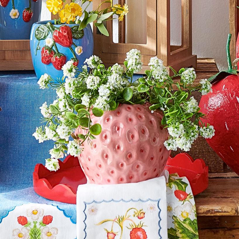 Decorative setting with strawberry-themed vases and plants on a table.
