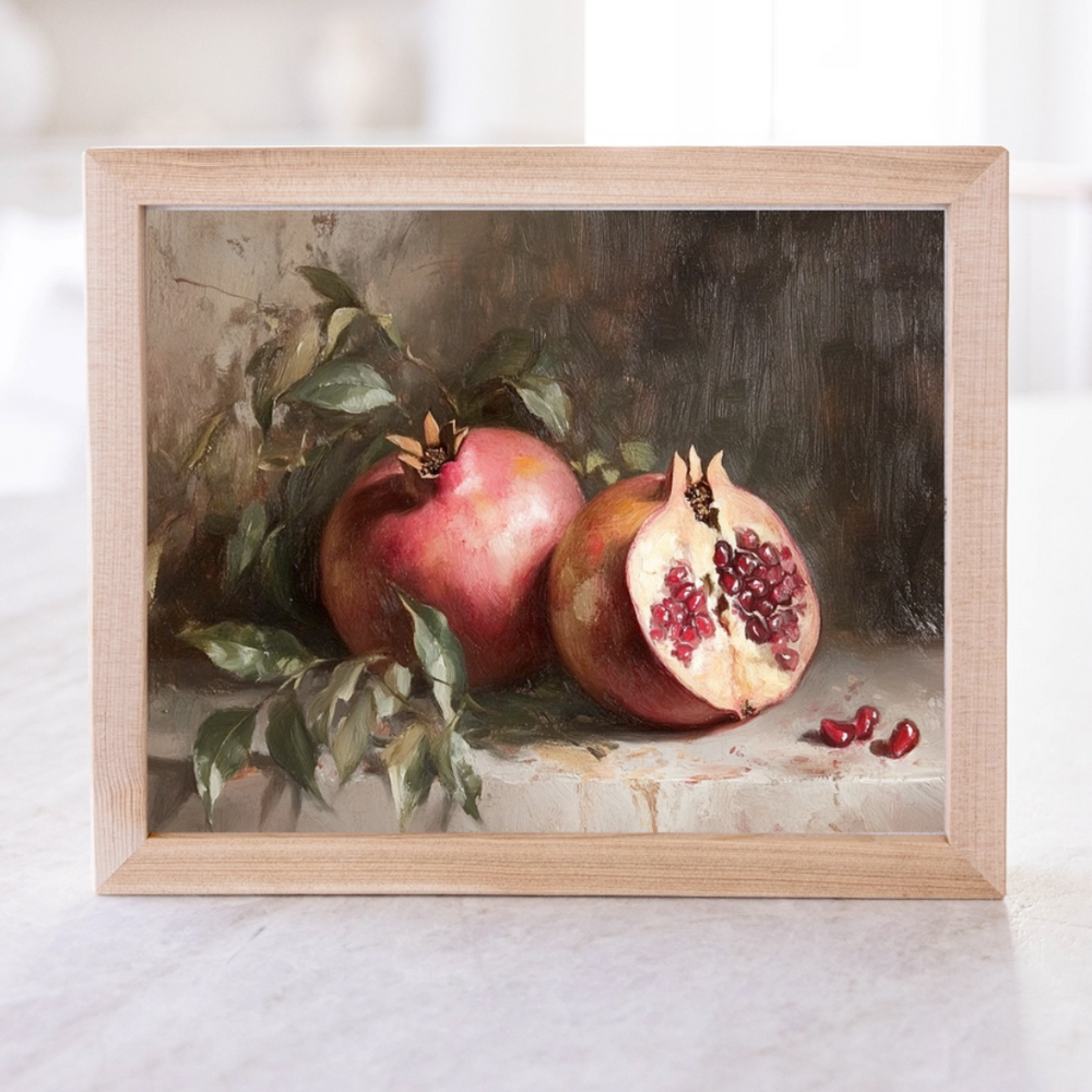 A framed artwork depicting a pomegranate cut in half with seeds scattered around, set against a dark background.