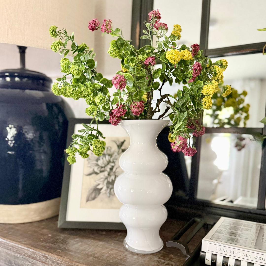 White vase with flowers on a wooden surface with decorative items.