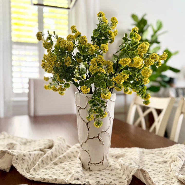 White vase with yellow flowers on a table in a bright room