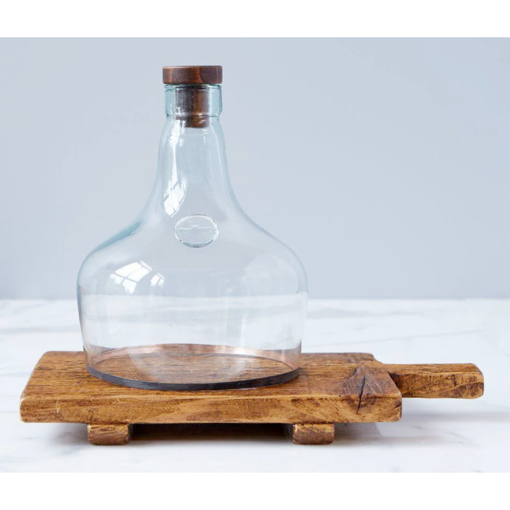 Clear glass carafe with wooden lid and base on a white surface