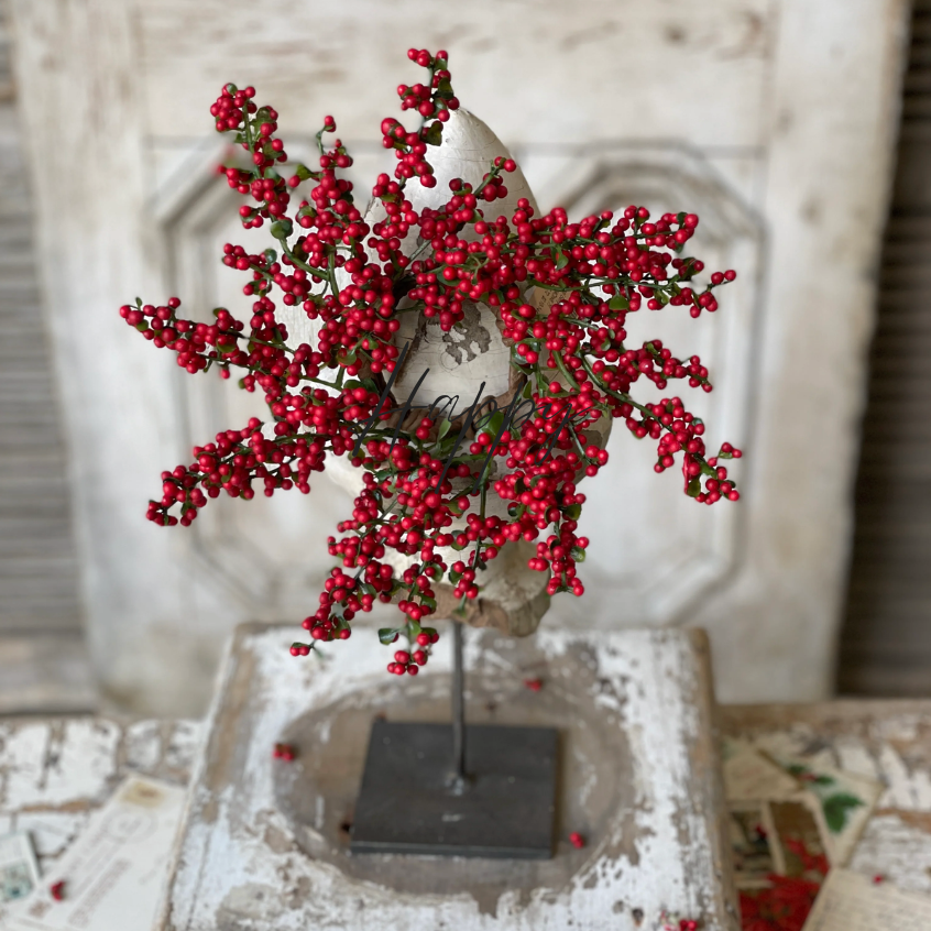 A red berry candle ring displayed on a candle, with bright red berries and small green leaves, placed on a rustic wooden surface.