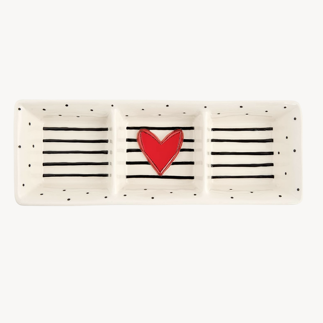 A divided stoneware serving dish with a white speckled background and a red heart shape in the center, with black horizontal stripes.