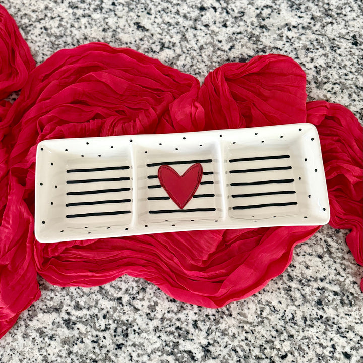 Stoneware divided serving dish with a red heart design on a red fabric background